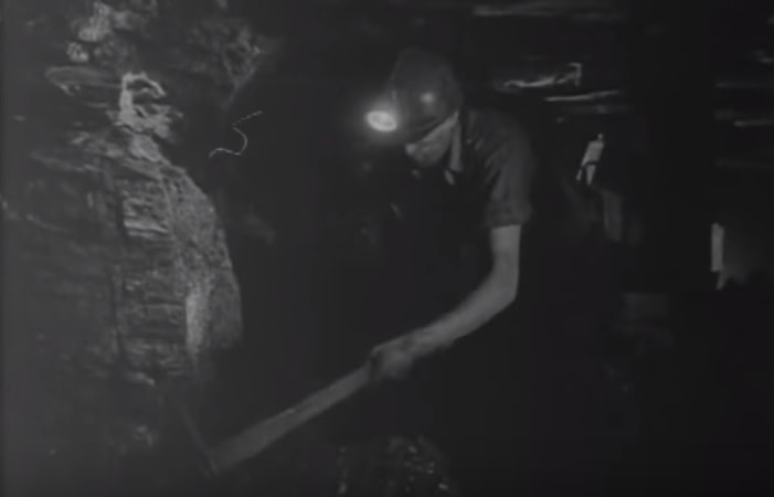 A coal miner digging for coal with a pick in an under ground dark mine