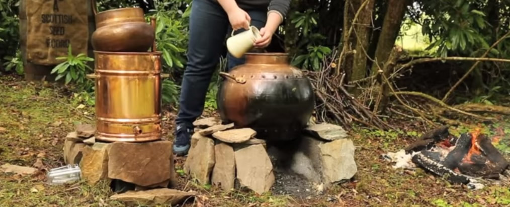 Man making Poitin in metal drums beside an open fire