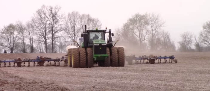 Green tractor tilling a field which has large wheels